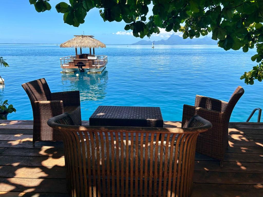 a table and chairs with a boat in the water at Moana Waterfront Bungalow in Punaauia