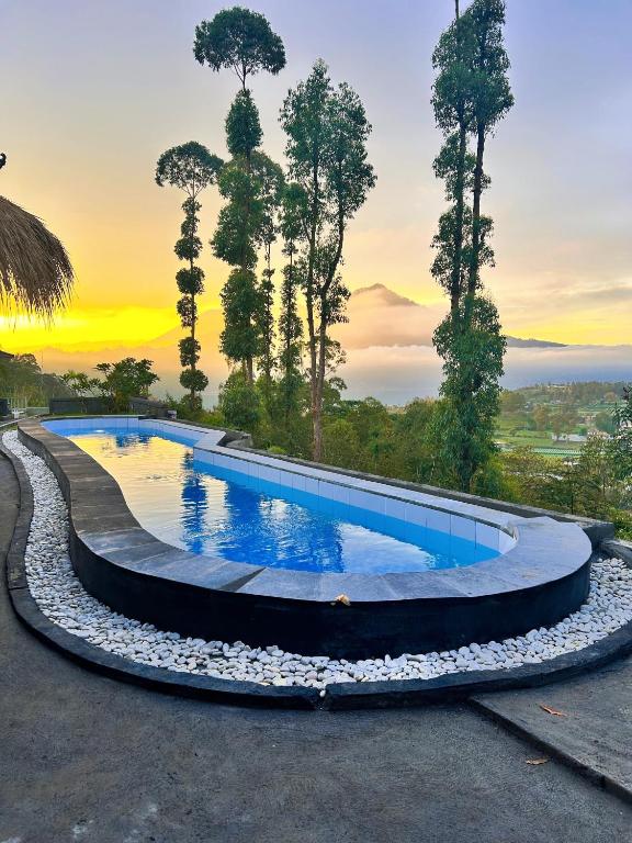 a pool with rocks around it with a sunset in the background at Pondok Bali Volcano in Kubupenlokan