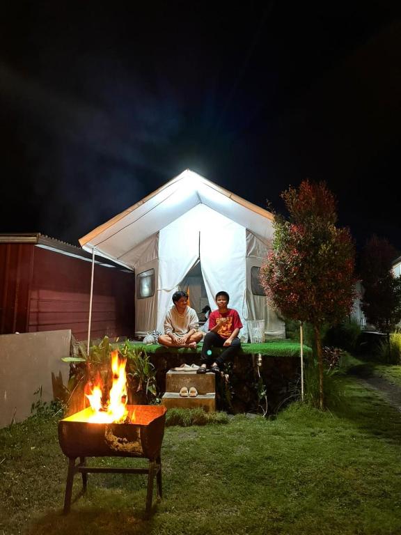 two people sitting in front of a tent with a fire at La Danu Glamping in Kubupenlokan