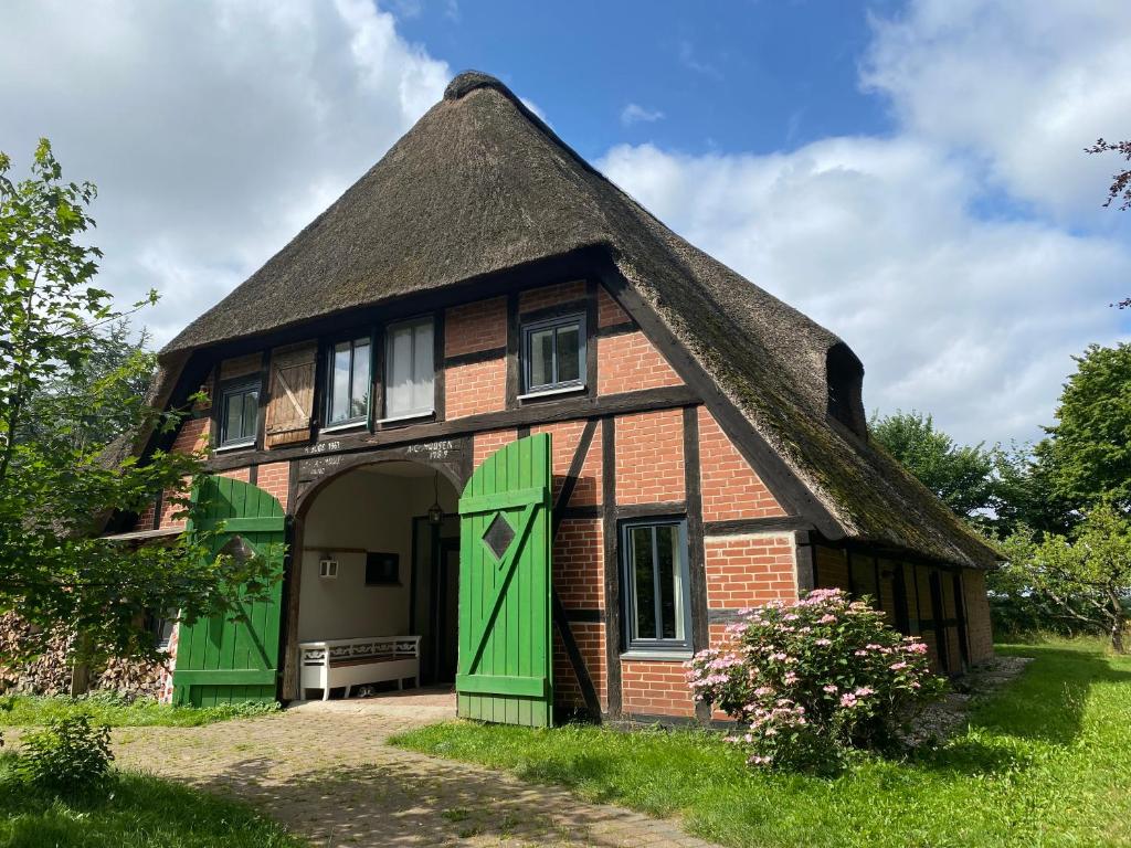 ein Haus mit einem Strohdach und grünen Türen in der Unterkunft Reet-Cottage Nahe der Ostsee in Süsel