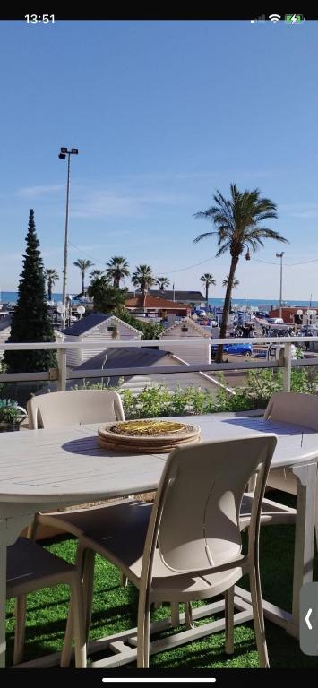 une table et des chaises blanches avec une table et des palmiers, dans l'établissement Studio vue splendide sur mer et port, à Saint Cyprien Plage