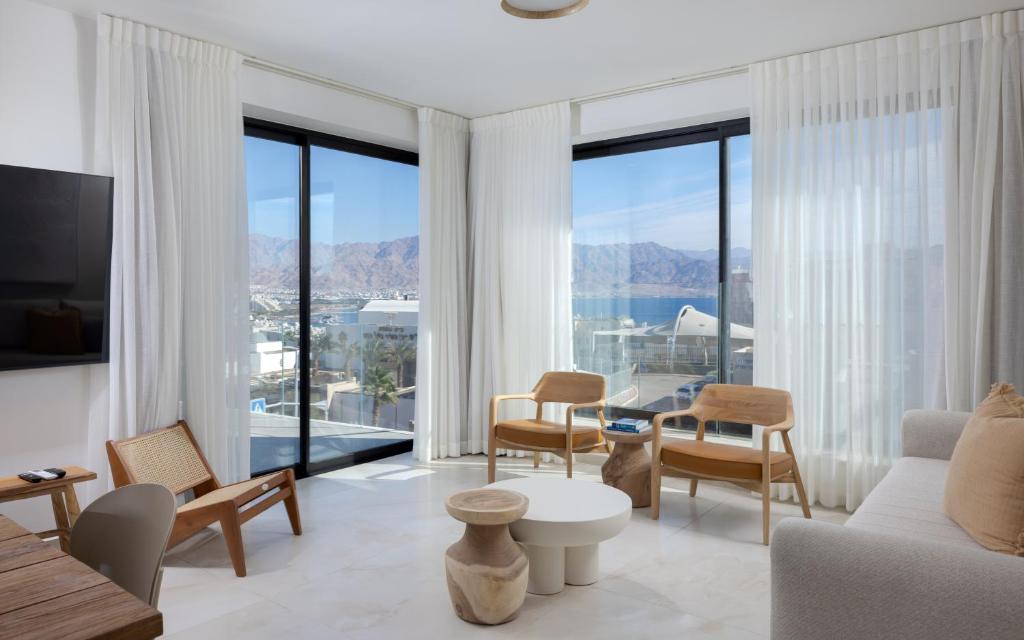 ein Wohnzimmer mit einem Sofa und Stühlen sowie großen Fenstern in der Unterkunft אורה דירות אירוח -נץ 9- דירות נופש איכותיות לנופש שקט ואקסלוסיבי in Eilat