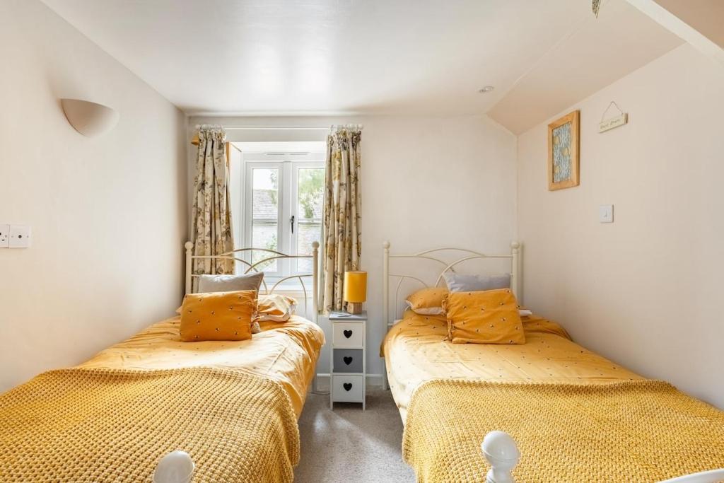 two beds in a room with yellow sheets at Blaise Cottage Cornwall in St Austell