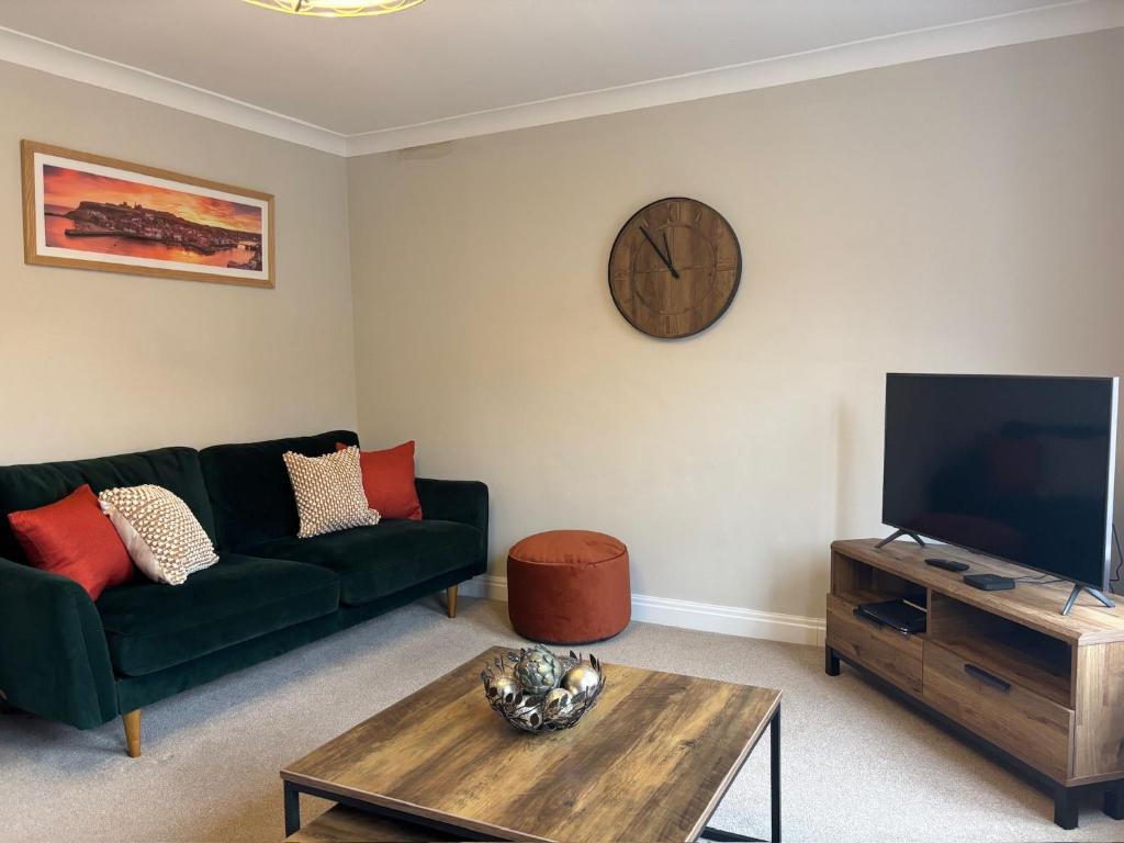 a living room with a green couch and a clock at Stylish & spacious harbour-view townhouse with parking in Whitby