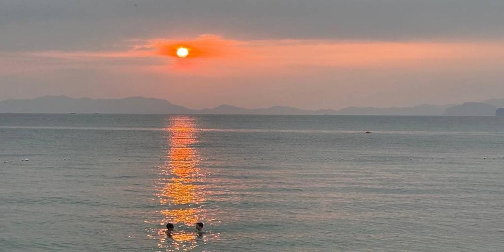 zwei Menschen schwimmen bei Sonnenuntergang im Meer in der Unterkunft Bliss Resort Krabi in Klong Muang Beach