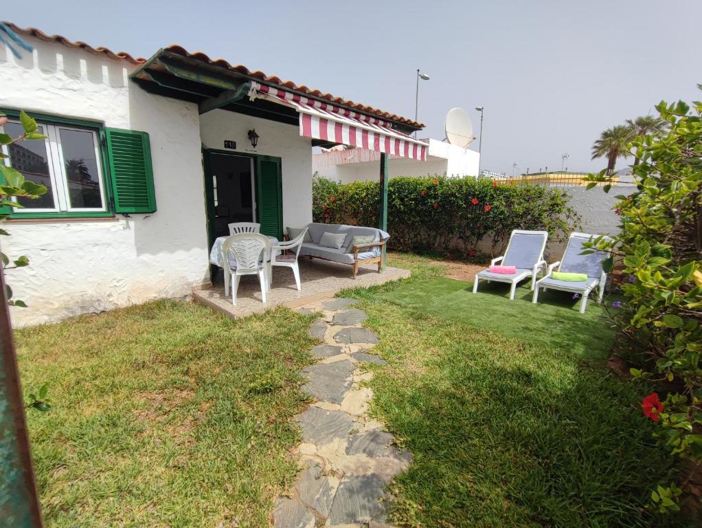 a yard with chairs and a table and a house at private Bungalow next to Yumbo Center in Playa del Ingles