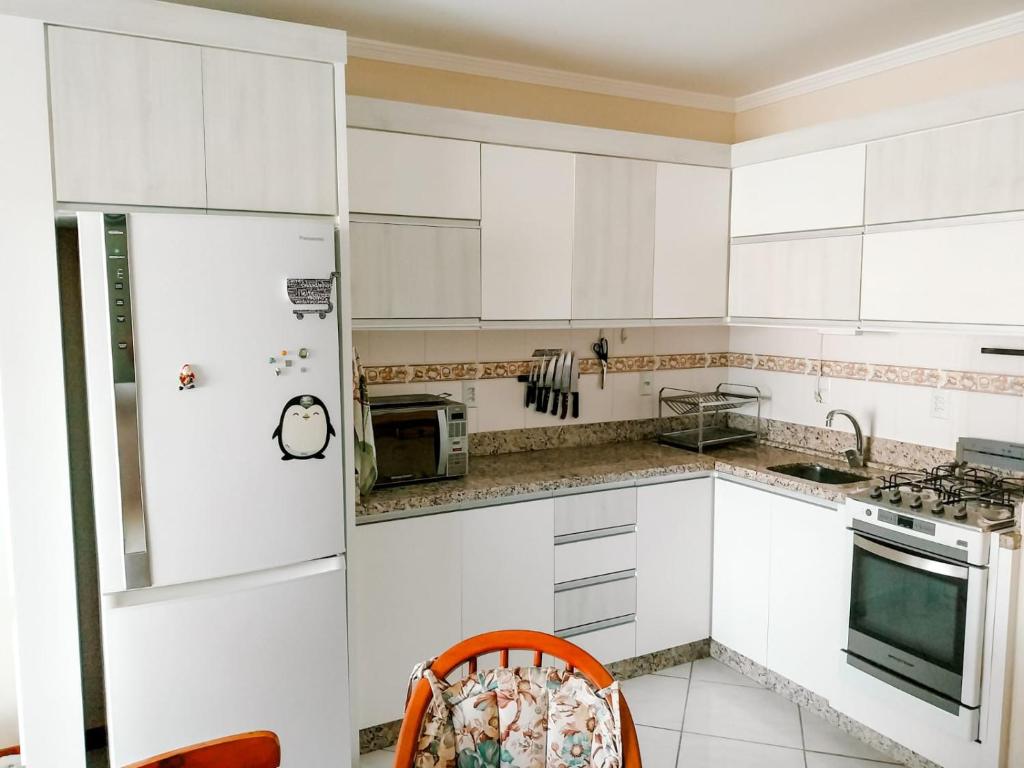 una cucina con mobili bianchi e un frigorifero di 3 quartos a 280m da praia c roupa de cama - Sacada com Churrasqueira - climatizado - 10 min a pé da passarela do Ribeiro e acesso a Praia de Bombinhas - 5 min a pé de supermercados - Até 8 pessoas, ideal p famílias, grupos, crianças a Bombas