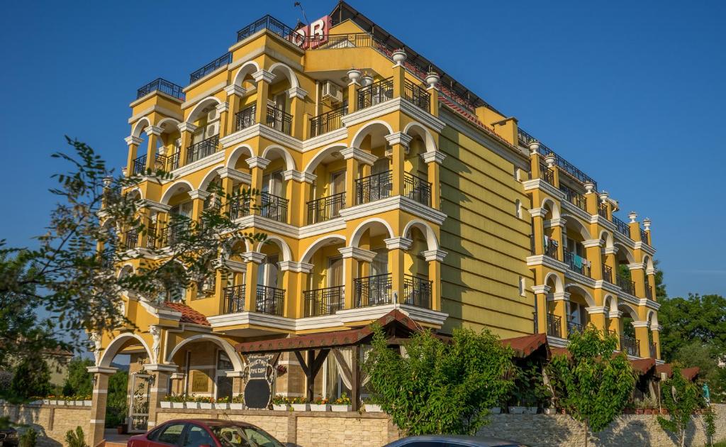 a yellow and white building with cars parked in front of it at Hotel Luxor in Lozenets