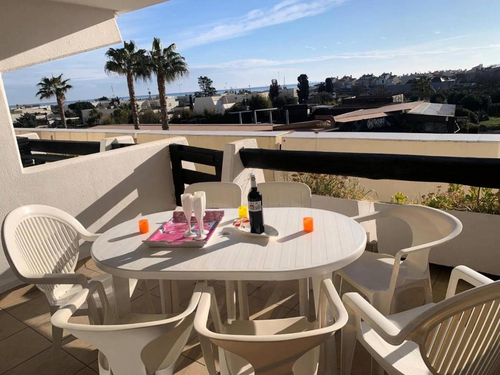- une table blanche avec une bouteille de vin sur le balcon dans l'établissement Résidence Port Nature Colline 5 - Port Nature Colline 5 - Appartement 4 personnes face Waiki MAE-6141, au Cap d'Agde