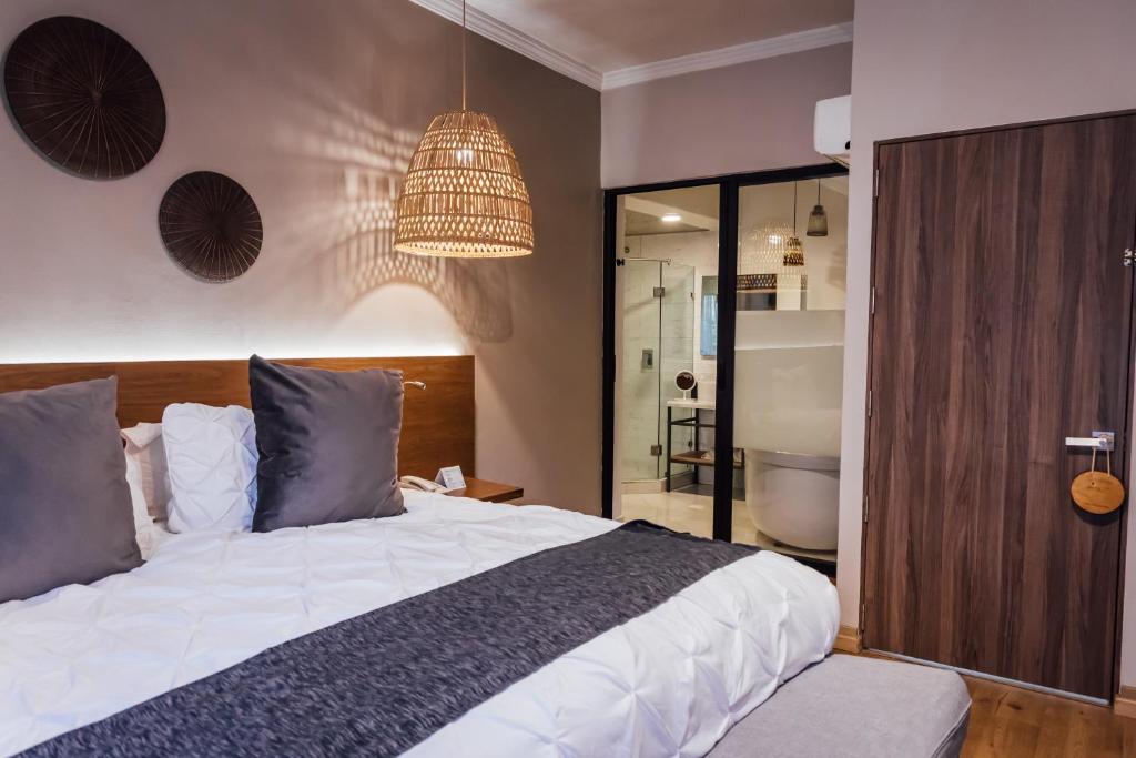 A warm-toned bedroom with a large bed, woven pendant light and glass-fronted bathroom.