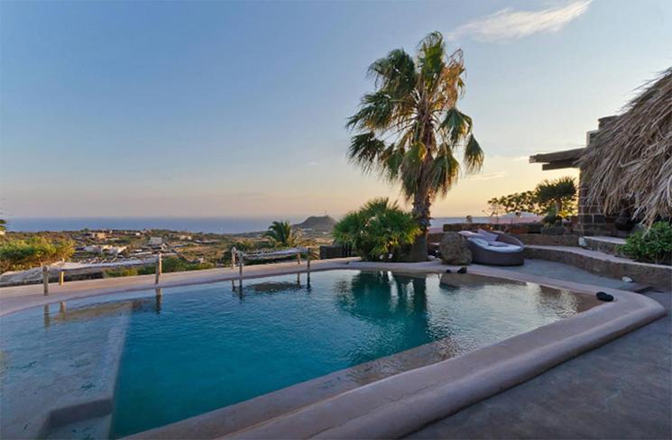 a swimming pool with a palm tree and a house at Dammusi Ambra in Pantelleria
