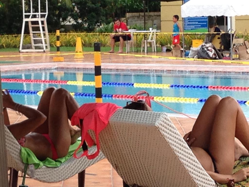 Dos personas sentadas en sillas junto a una piscina en Chateau Elysee, en Manila