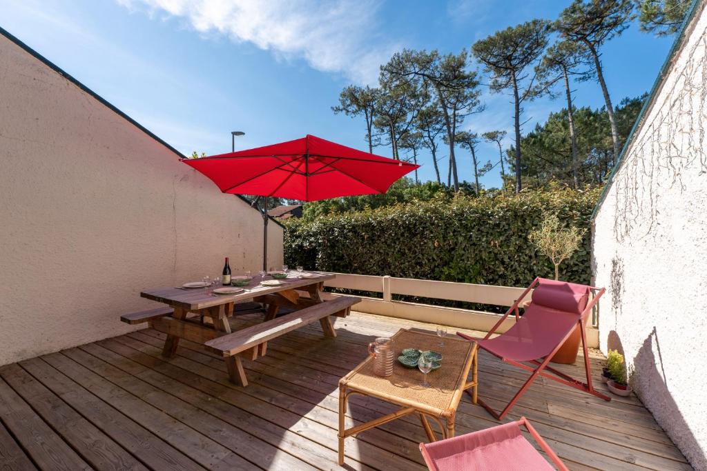 une terrasse en bois avec une table et un parasol rouge dans l'établissement Villa Xarma 7 Pers Proche Plage, à Seignosse