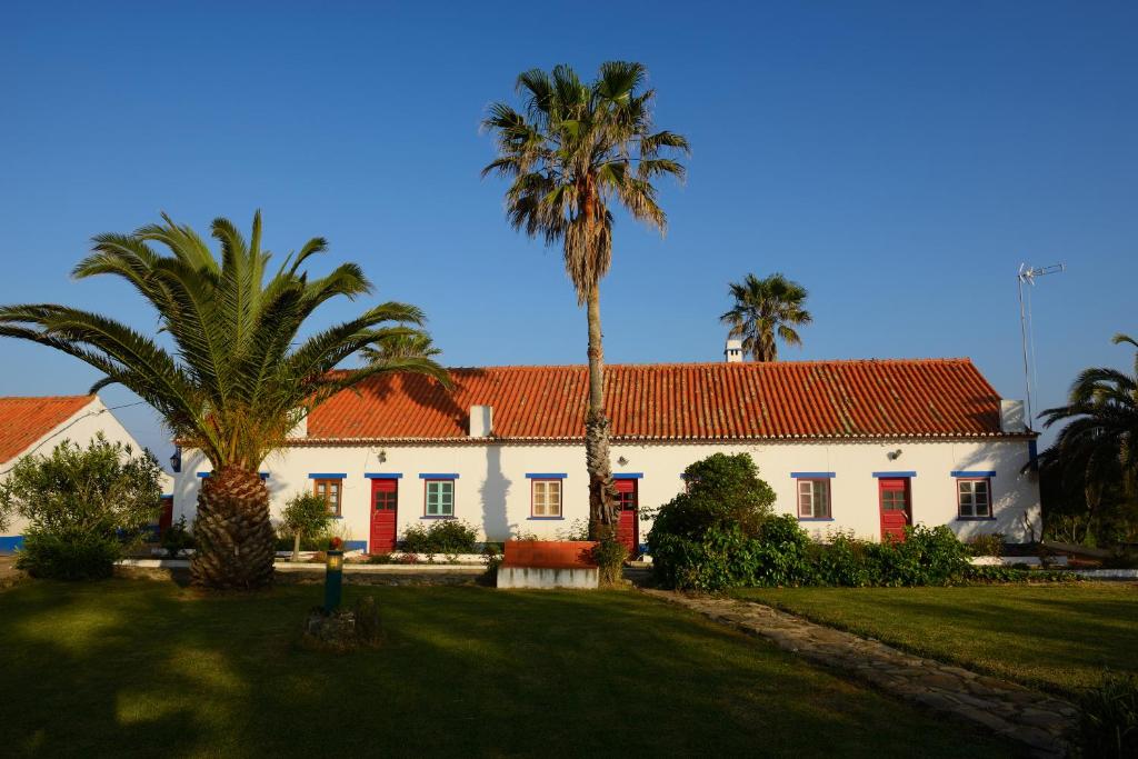 a white house with red doors and palm trees at Herdade Do Pessegueiro in Porto Covo