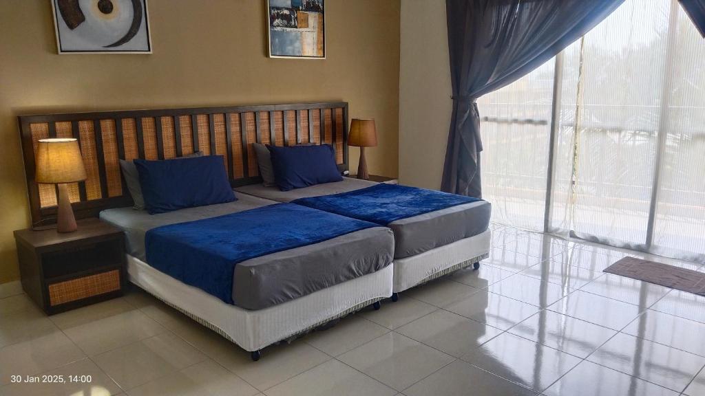 a bedroom with a bed with blue sheets and a window at CStone Legacy Gold Coast Morib Resort in Banting