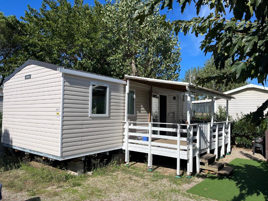 Une petite maison blanche avec une véranda et une clôture dans l'établissement Mobil Home 3 chambres dans camping 4 étoiles, à Vias