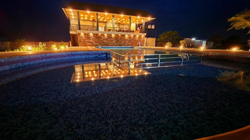 a building with lights in front of a swimming pool at night at Tathastu Farms & Resort in Kota