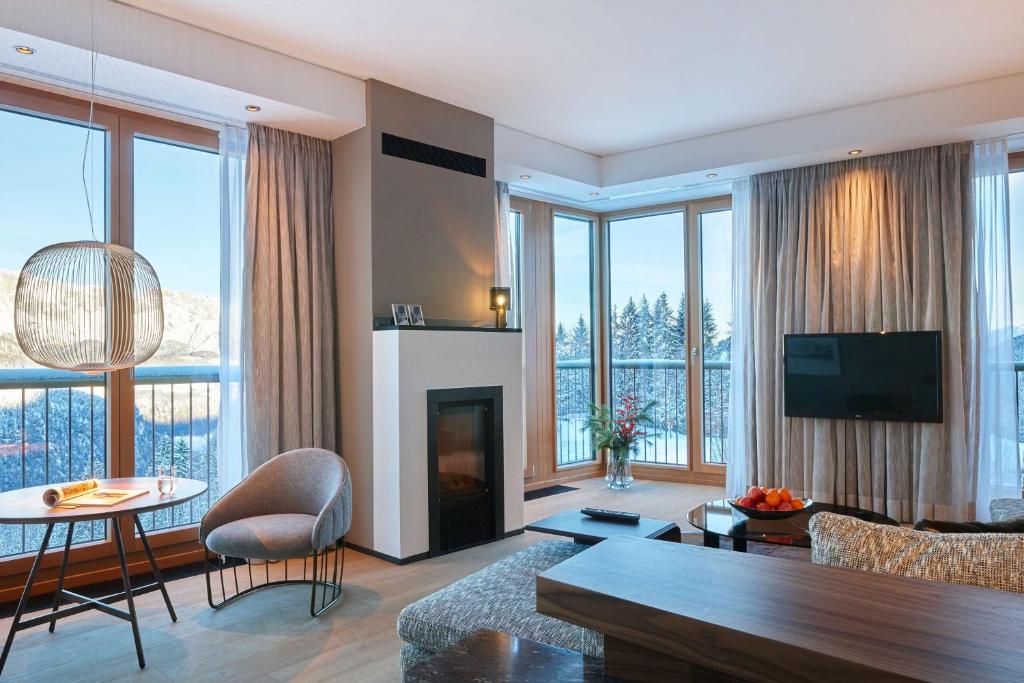 a living room with a fireplace and large windows at Kempinski Hotel Berchtesgaden in Berchtesgaden