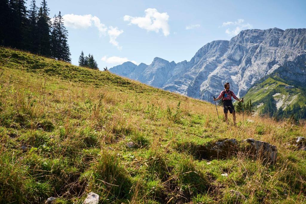 a person walking on a grassy hill with mountains in the background at Kempinski Hotel Berchtesgaden in Berchtesgaden