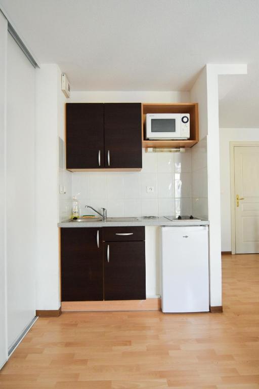 a kitchen with black cabinets and a white refrigerator at Residhotel Mulhouse Centre in Mulhouse