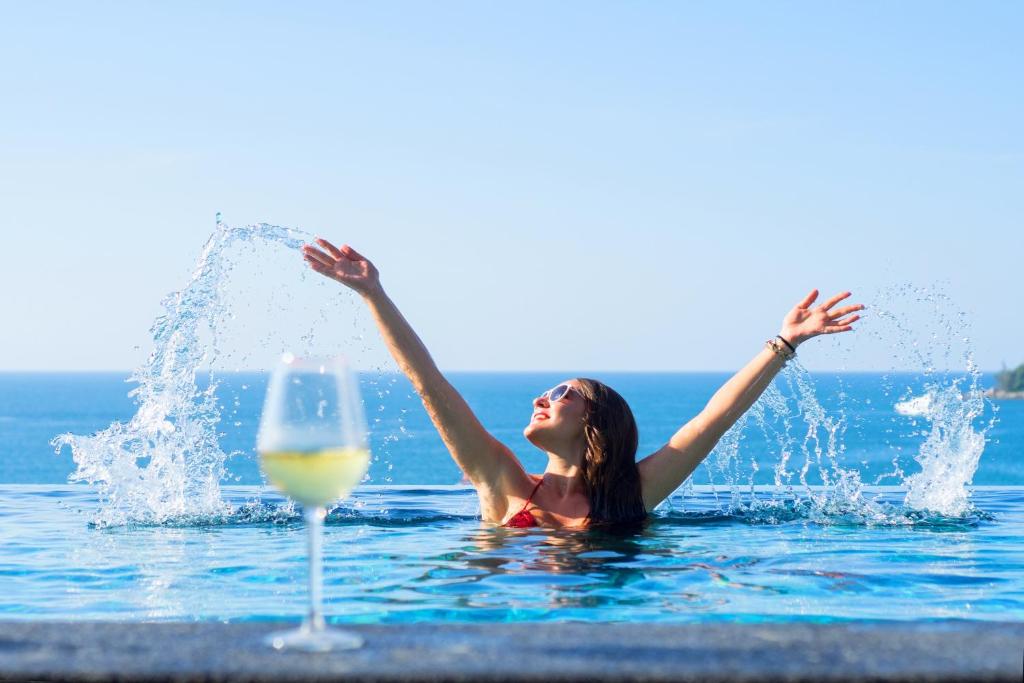 een vrouw in het water met een glas wijn bij Norn Talay Surin Beach Phuket in Surin Beach