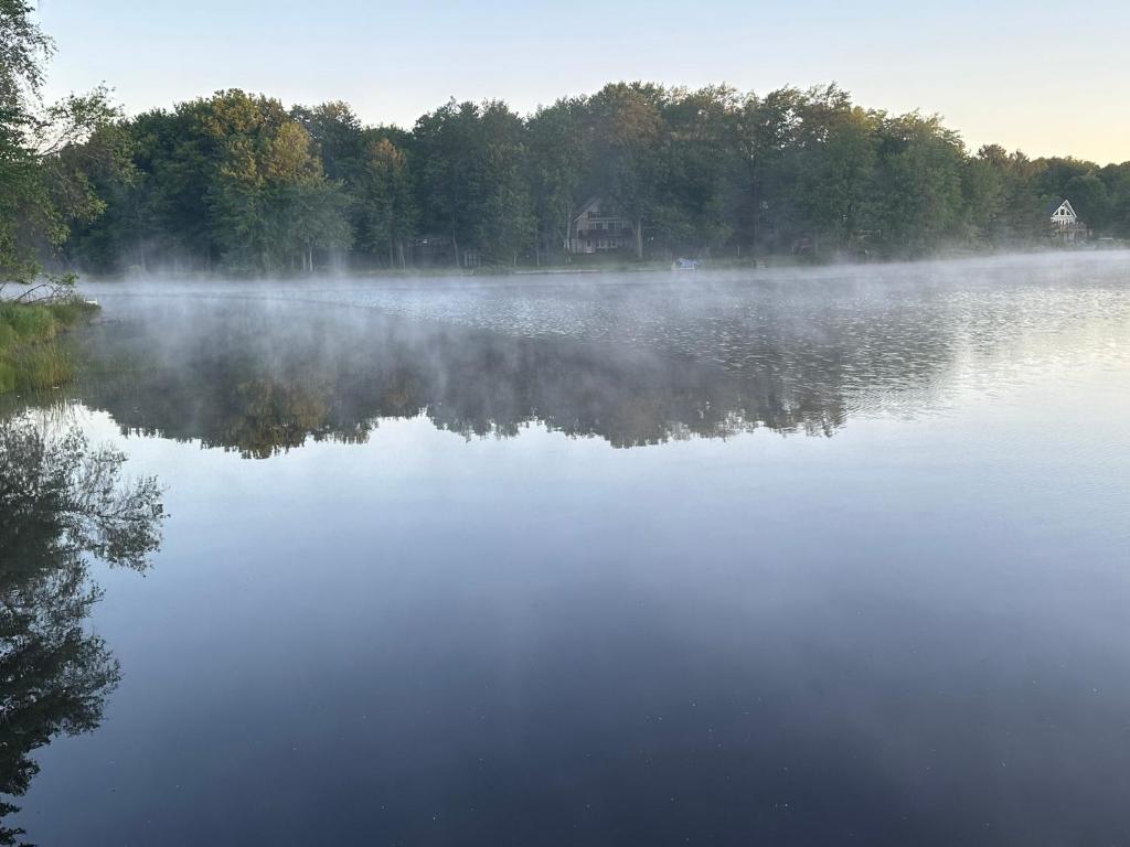 un lago nebuloso con una casa en el fondo en Peaceful Pocono Lakefront, beach, pools, firepit, pets, en Arrowhead Lake