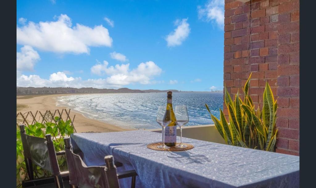 a bottle of wine sitting on a table next to the beach at 3 bedrooms with Views over Kirra! in Gold Coast