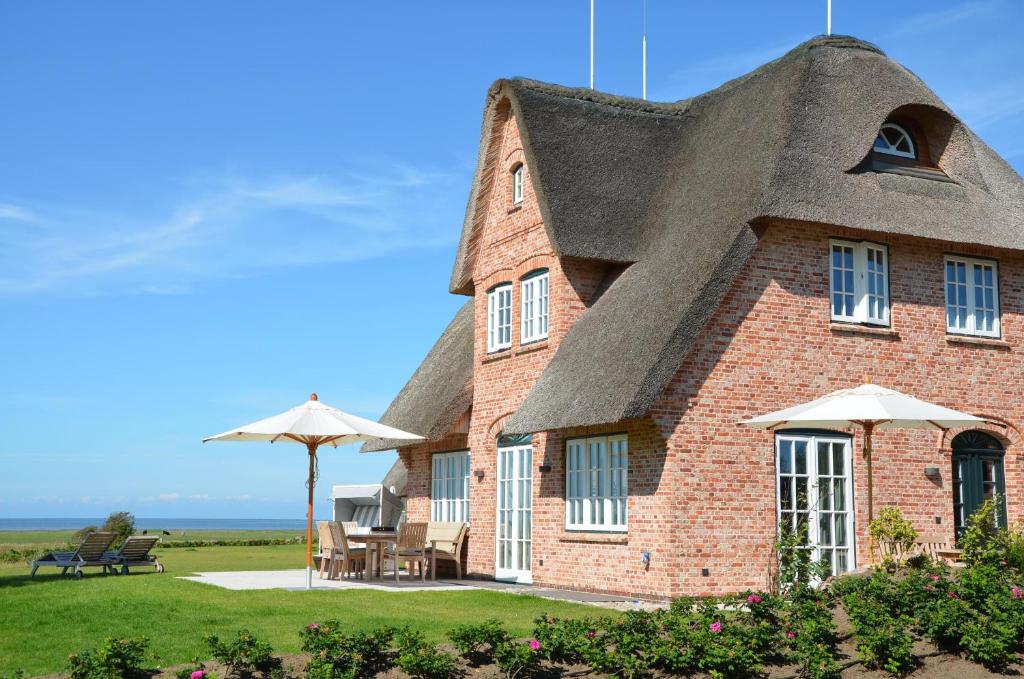 a house with a thatched roof with chairs and an umbrella at LITZKOW 12808 in Westerwall