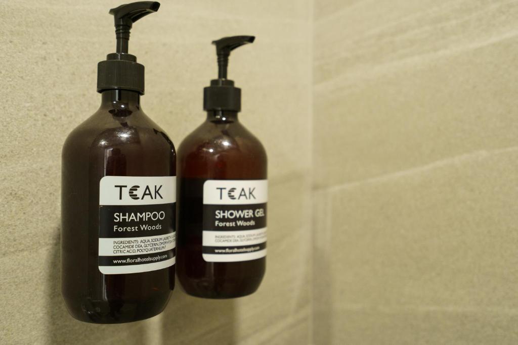 Wall-mounted TEAK Forest Woods shampoo and shower-gel dispensers in a tiled bathroom.