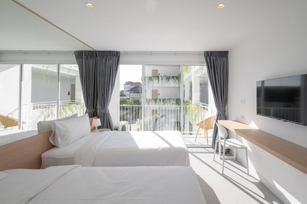 A sunlit twin room with two beds, a large glazed opening and a small balcony with outdoor chairs.