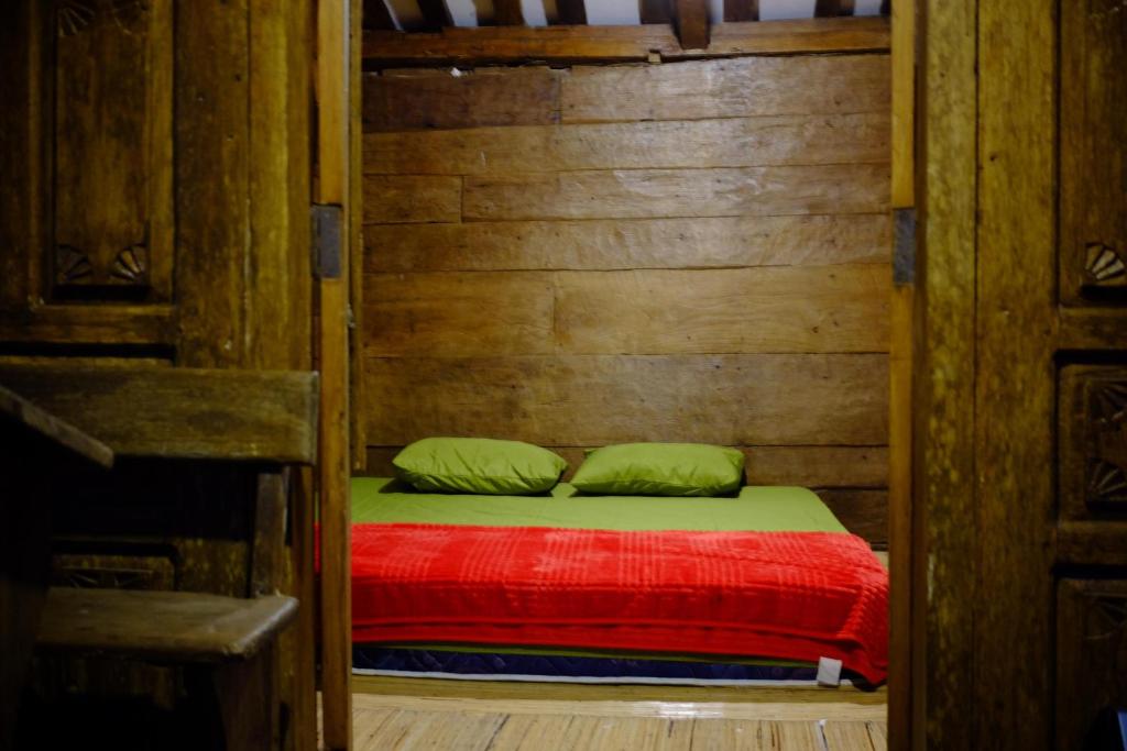 a small bed with a red blanket and green pillows at Sang Natha Lodge in Tjatur
