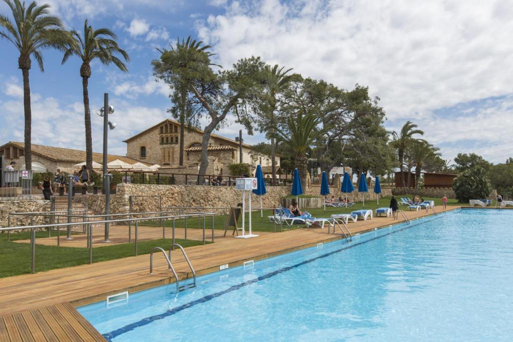 a large swimming pool with blue umbrellas and palm trees at Glamping Costa Dorada in Vilanova i la Geltrú