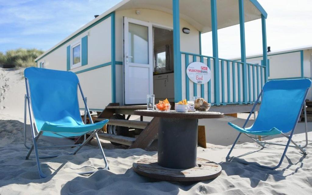zwei Stühle und ein Tisch im Sand in der Nähe eines winzigen Hauses in der Unterkunft Vlugtenburg in s-Gravenzande