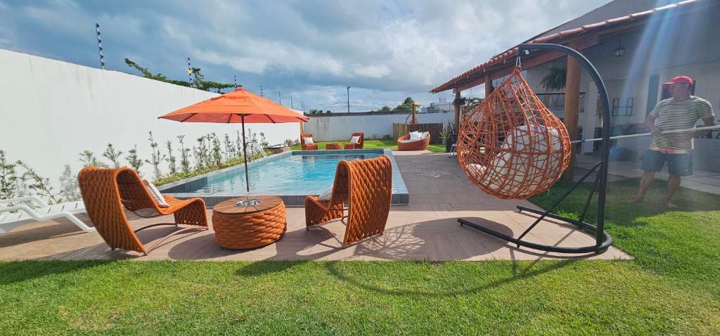 un hombre de pie junto a una piscina con un columpio y una sombrilla en Pousada Alkamar, en Maragogi