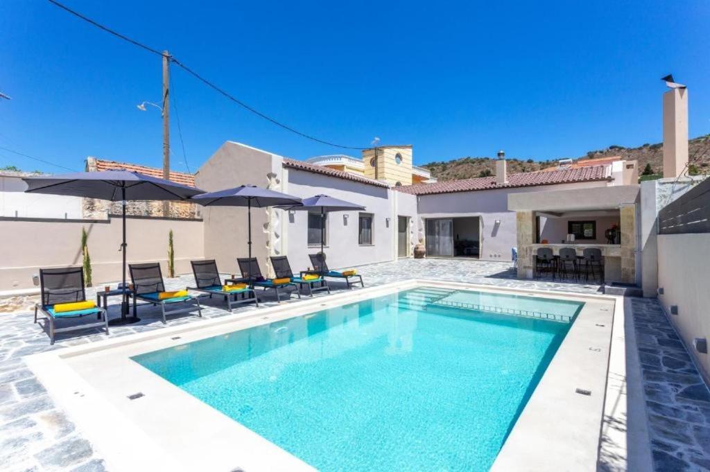 a pool with chairs and umbrellas next to a house at Villa Archontiki in Kalamítsion Alexándrou