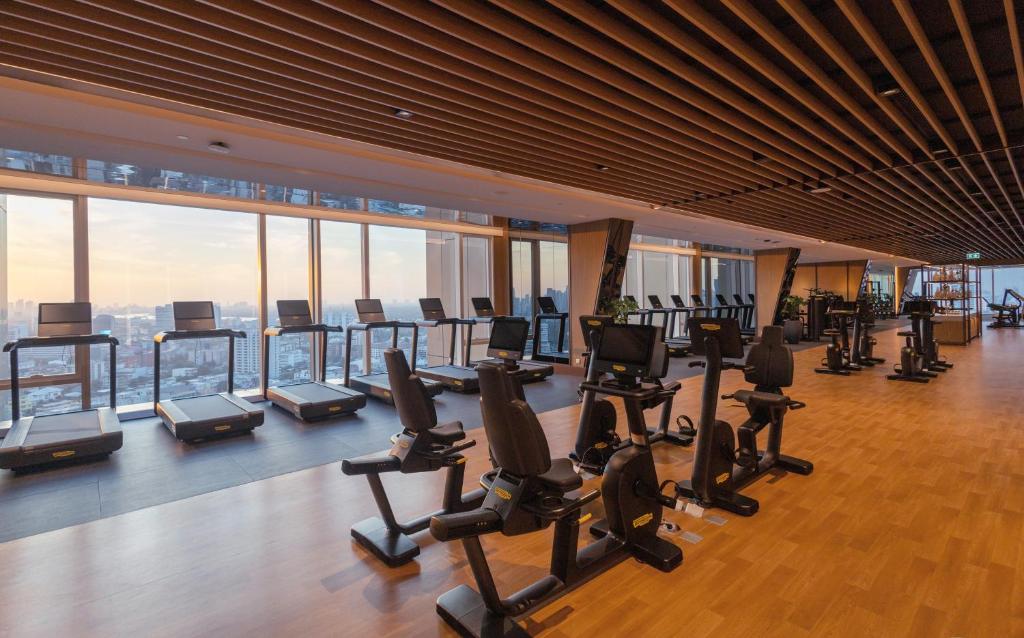 A panoramic cardio room with treadmills and reclining bikes beside skyline windows.