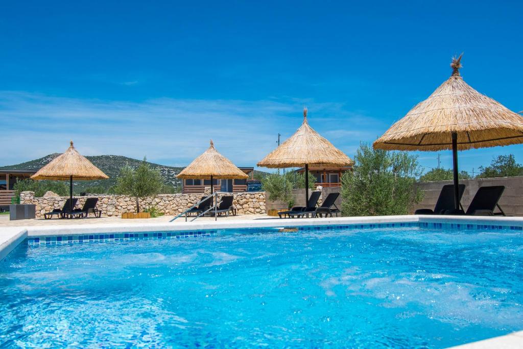 a swimming pool with chairs and umbrellas at Mobile home Banovi dvori III in Tisno