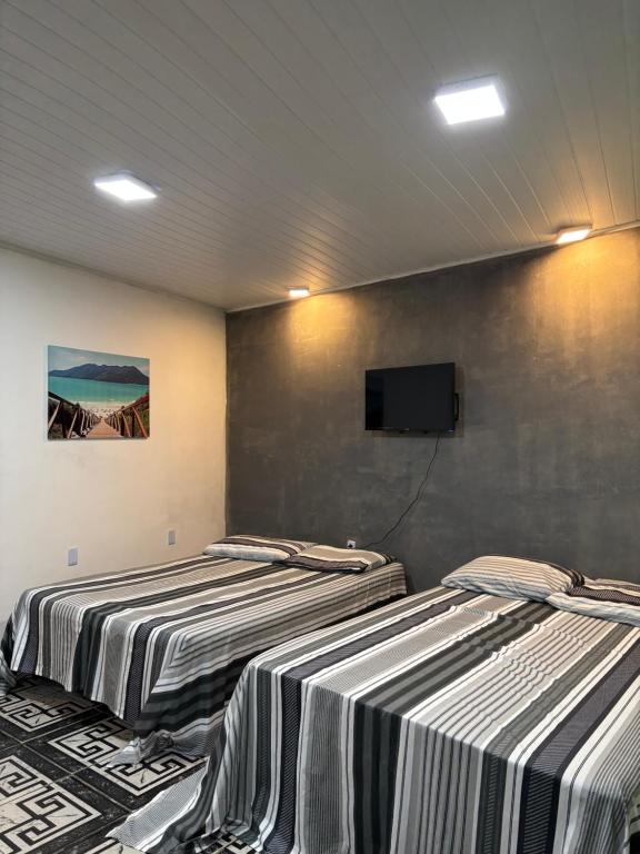 deux lits dans une chambre avec une télévision au mur dans l'établissement Kitnet Maria Bonita - Cabo frio, à Cabo Frio