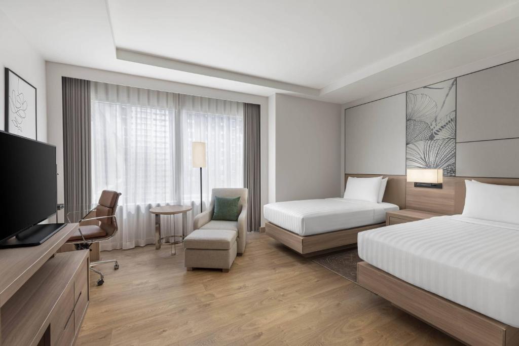 A spacious-looking room with two beds, a work desk and an upholstered chaise.