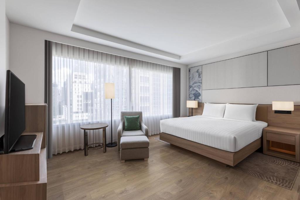 A king-bed room with a lounge chair, television and large city-facing window.