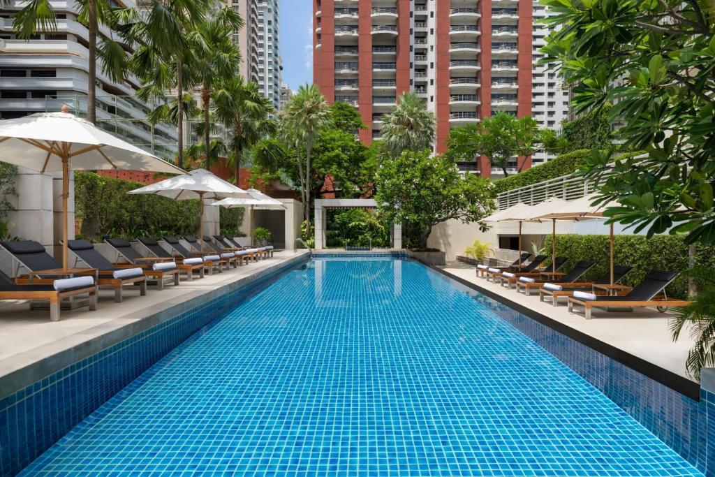 A long rooftop-style pool lined with loungers and umbrellas among high-rise buildings.