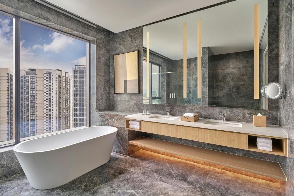 A marble-finished bathroom with a freestanding tub, double vanity, and large city-facing window.