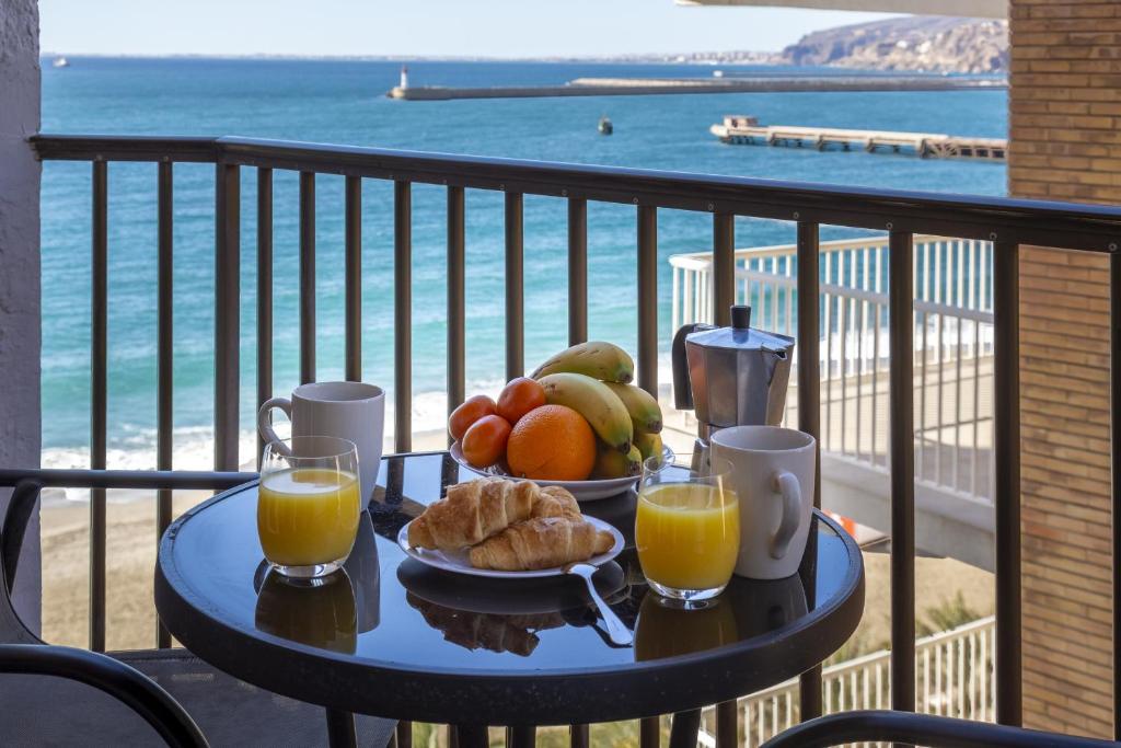 a table with a plate of fruit and orange juice on a balcony at AlmeriaSuite Impressive Beach Views in Almería