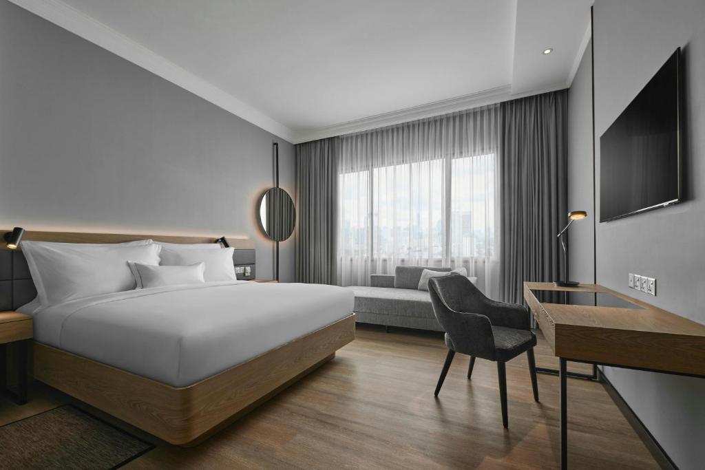 A contemporary guest room with a large bed, desk, sofa, and wall-mounted television.