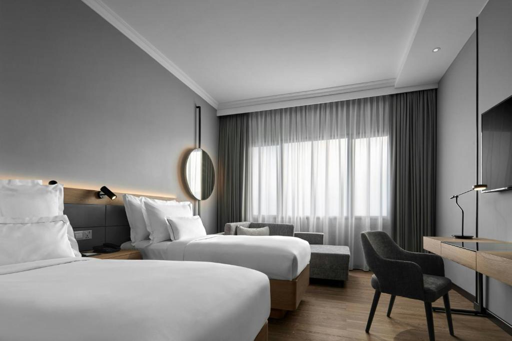 A bright twin room offers two beds, a sofa, and a separate desk area.