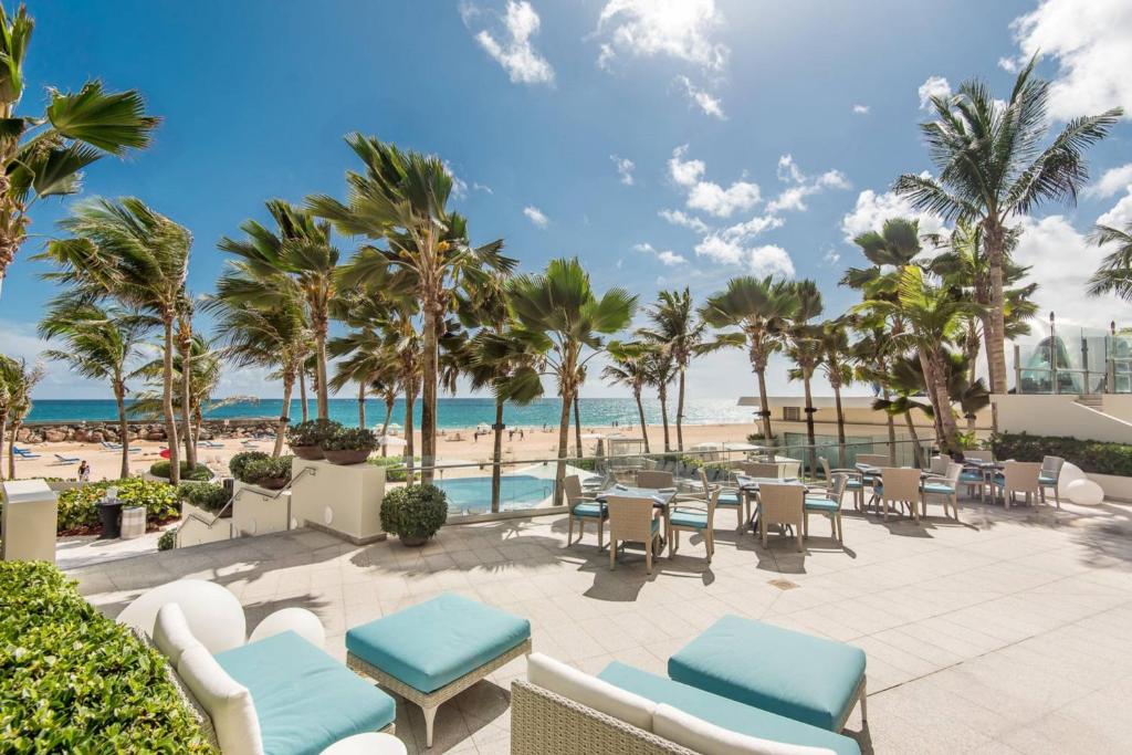 un patio sulla spiaggia con tavoli, sedie e palme di La Concha Resort, Puerto Rico, Autograph Collection a San Juan