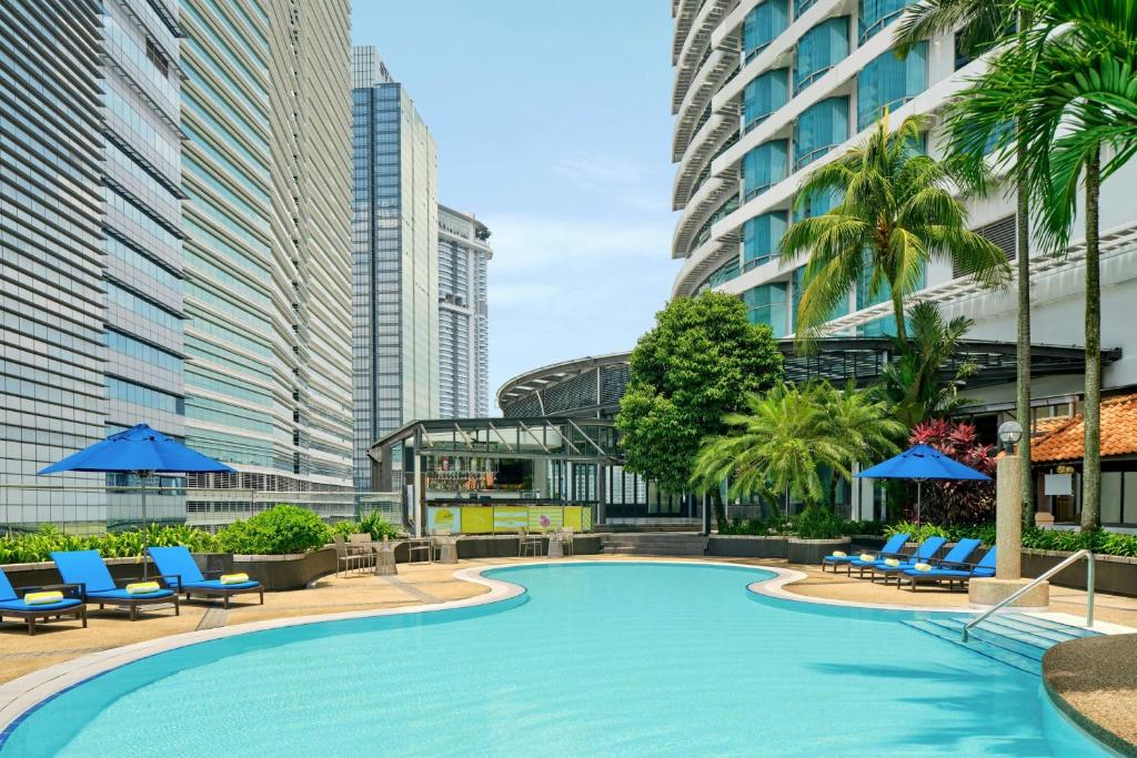 a swimming pool with chairs and palm trees and buildings at Le Méridien Kuala Lumpur in Kuala Lumpur