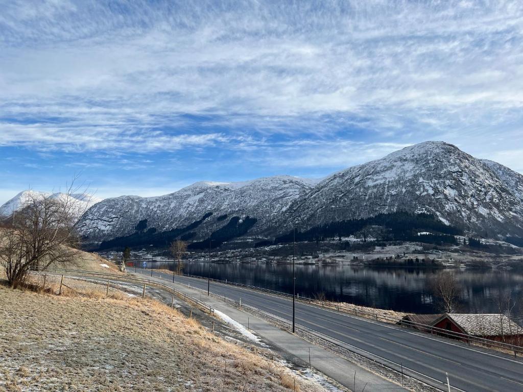 a road with snow covered mountains and a body of water at Husslåttene apartments in Skei