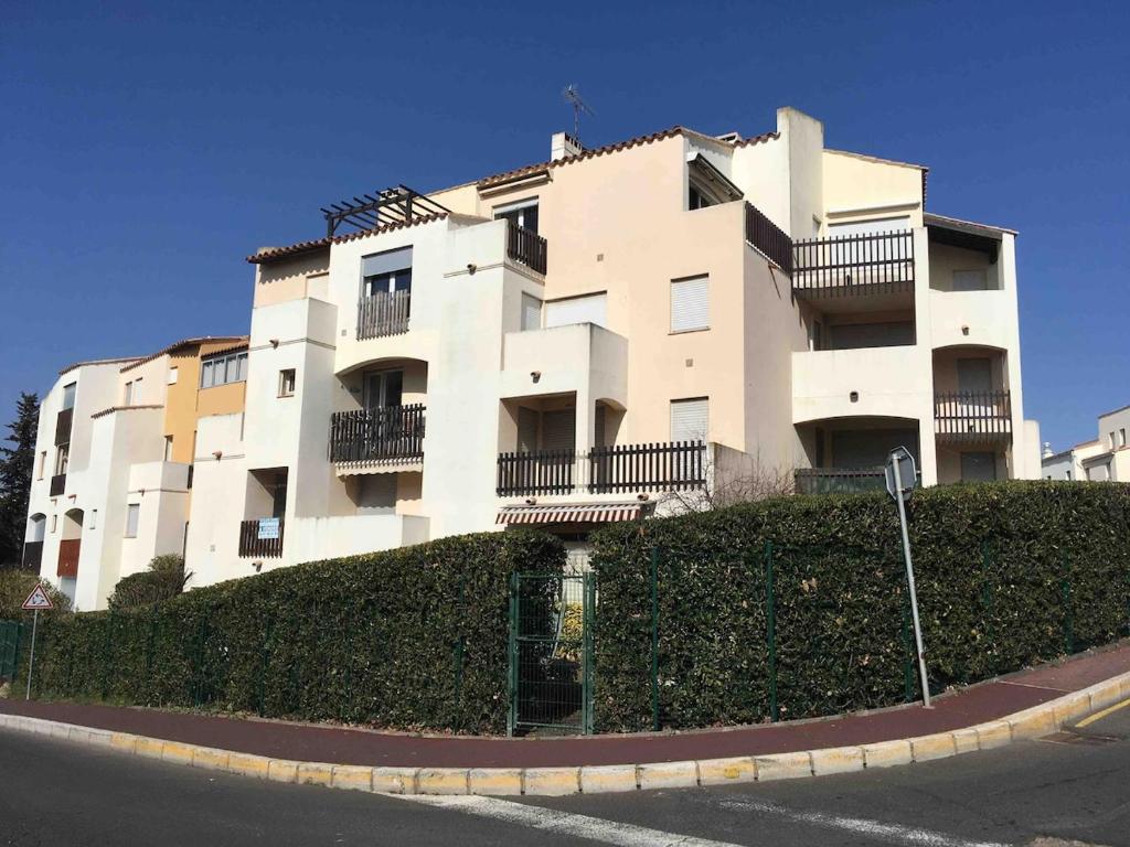un grand bâtiment blanc au sommet d'une haie dans l'établissement Studio avec parking clim Cap d Agde, au Cap d'Agde