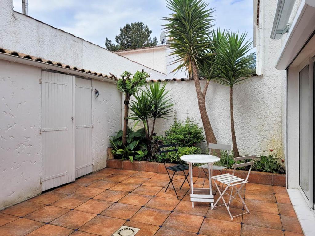 d'une terrasse avec une table, des chaises et des palmiers. dans l'établissement Maison 4 pièces à étage - Proche mer - Patio, BBQ - Parking - FR-1-705-94, aux Mathes